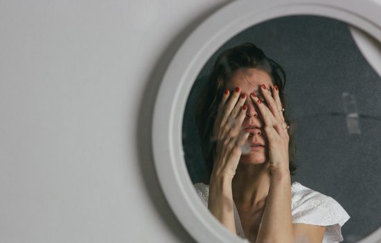 reflection of woman covering her face with her hands; the mirror is cracked making part of her reflection doubled - co-occurring diagnoses