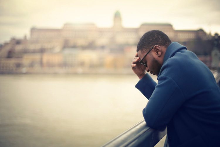 handsome Black man looking sad standing on bridge thinking - seasonal depression