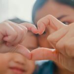 woman and her child holding up their hands together into a heart shape