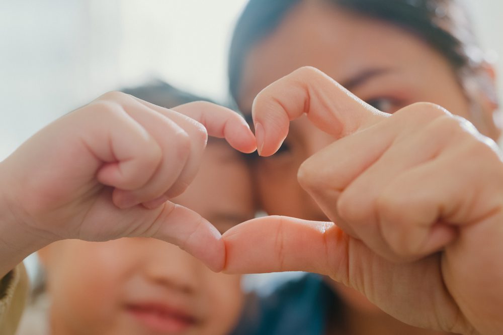 woman and her child holding up their hands together into a heart shape