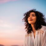 Woman standing outdoors at sunset with a soft smile and peaceful expression, symbolizing gratitude, hope, and emotional well-being.