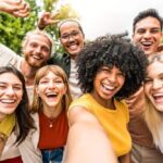 Group of diverse young adults smiling and posing closely together for a selfie outdoors, expressing joy, connection, and positive summer energy.