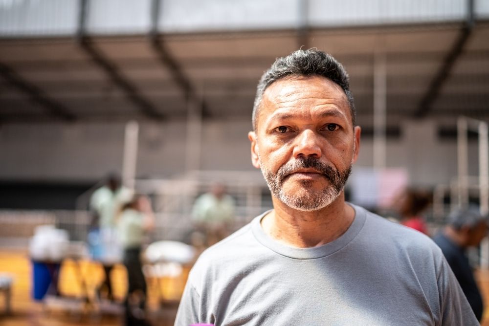 Portrait of a middle-aged man standing indoors with people and supplies in the background.
