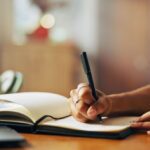 A woman diligently writing notes in a notebook, surrounded by a calm environment.