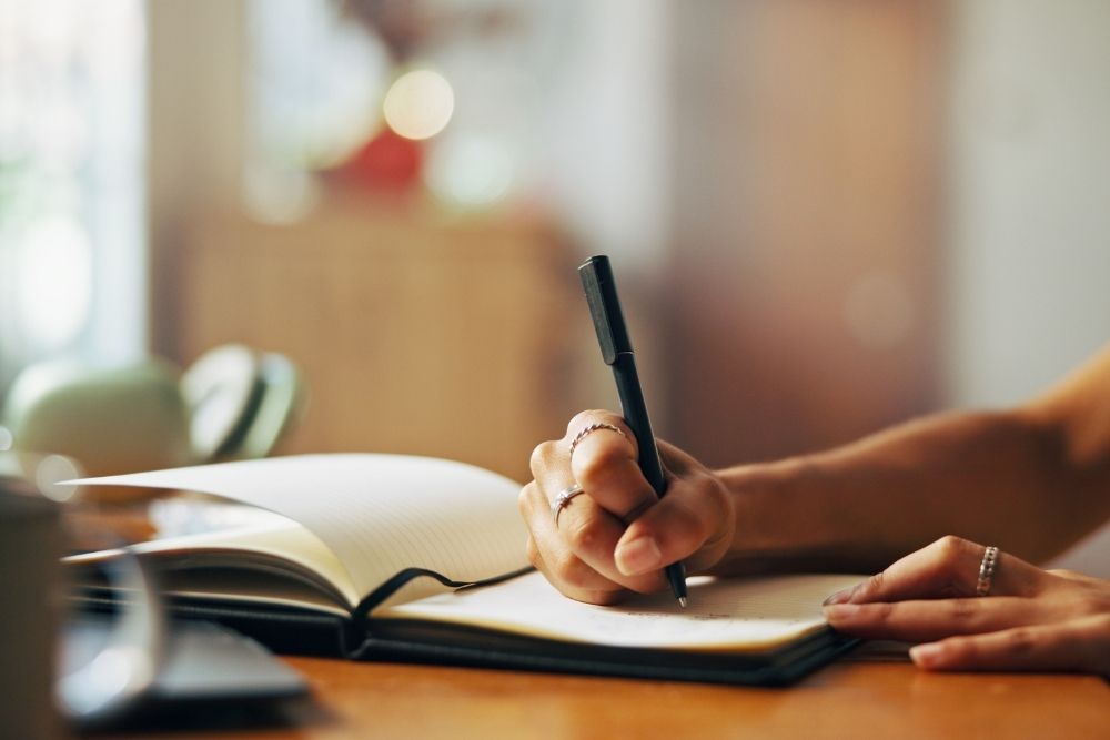 A woman diligently writing notes in a notebook, surrounded by a calm environment.