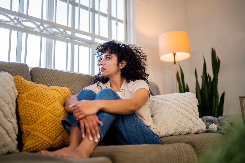 Highland Hospital - Red Flags for Behavioral Health Disorders - Edited. A woman sits on a couch looking out into the distance from a window.
